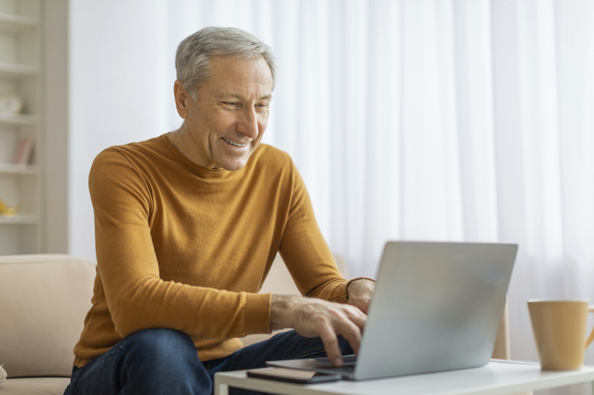 Older man happily working on laptop at home